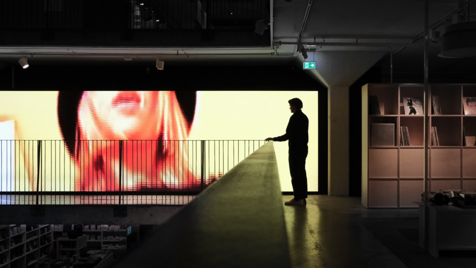 Die Silhouette einer Person, die im IKEA Museum steht und auf einen großen Bildschirm guckt, der eine Frau beim musikalischen Hörgenuss zeigt.