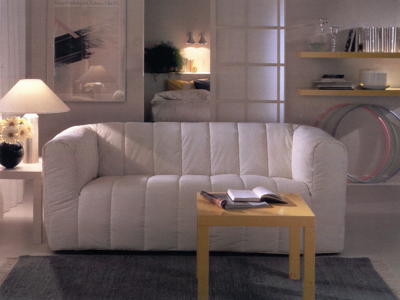 A room in white with a plump white KLIPPAN sofa in the middle. A coffee table and wall shelves in light wood, model LACK.