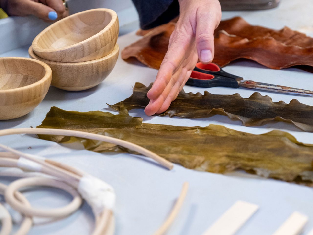 Närbild av händer under en workshop, olika material utspridda på bordet.